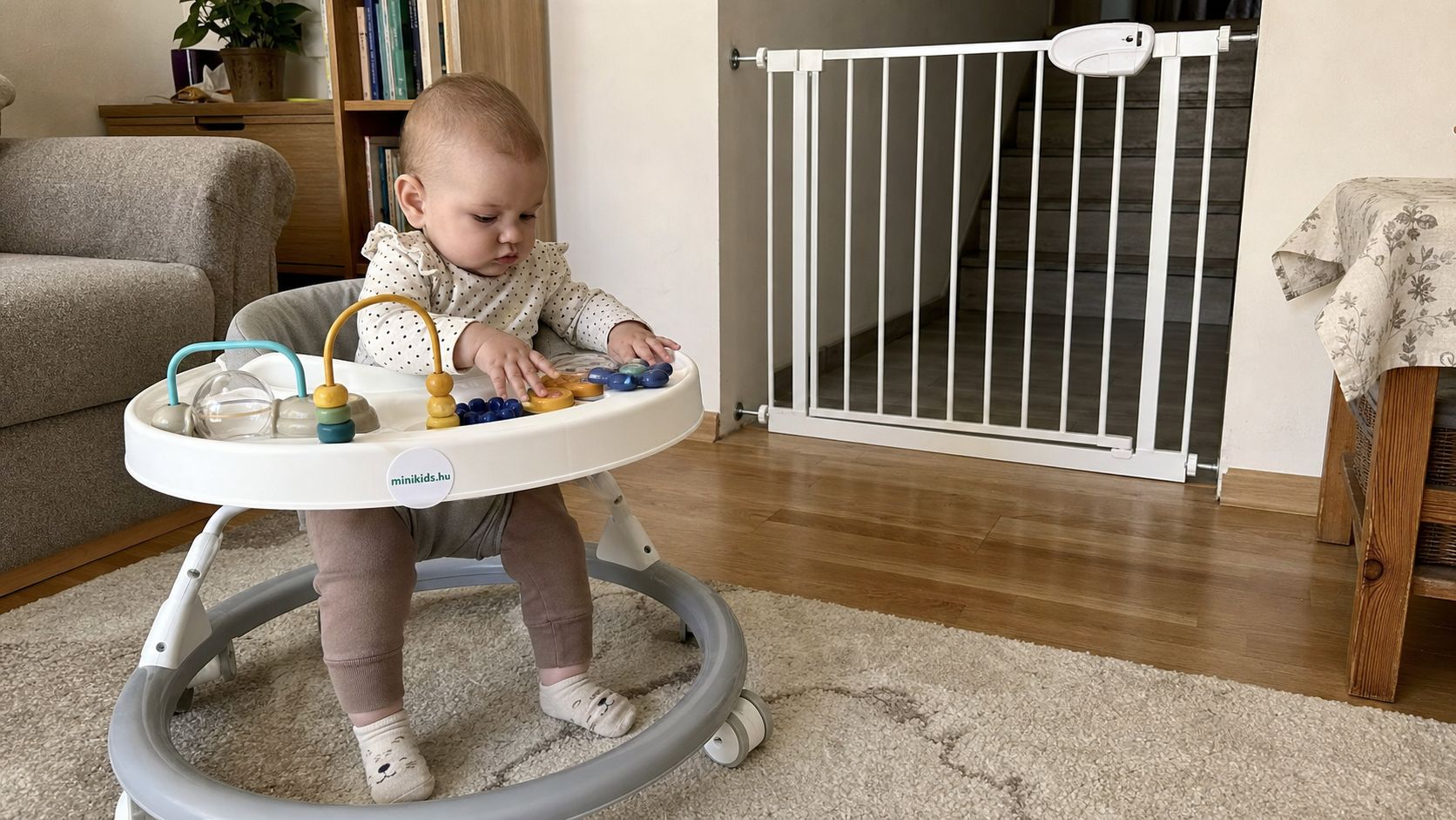 Bébikompban ülő baba a nappaliban, a háttérben a lépcsőfeljárót zárt biztonsági kapu védi