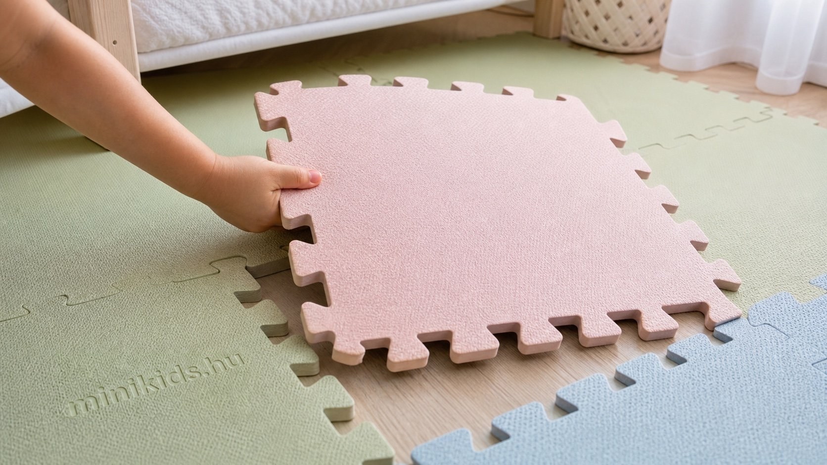 Kisgyerek keze illeszt egy nagy, pasztellszínű puzzle habszőnyeg-elemet a helyére a gyerekszoba padlóján